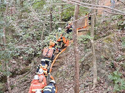 ホースを担いで山を登る消防隊員らの写真