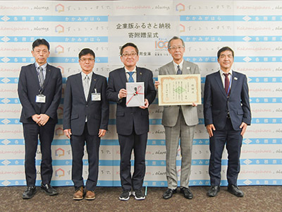 寄附目録と感謝状を手に持ち記念撮影を受ける浅野市長と小川理事長と関係者の写真