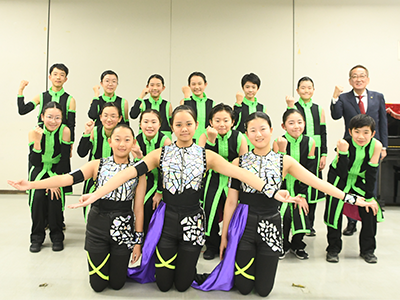 演奏のテーマの決めポーズをしながら記念撮影を受けるかかみの音楽フォレストさくらマーチングバンドメンバーと浅野市長の写真