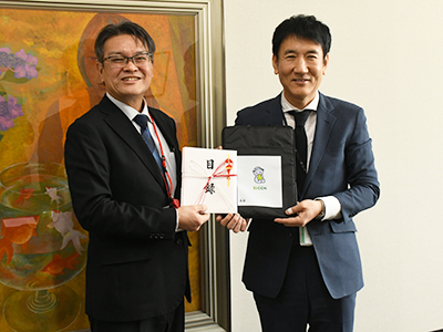 寄贈品を持って並ぶ河合校長と泉取締役