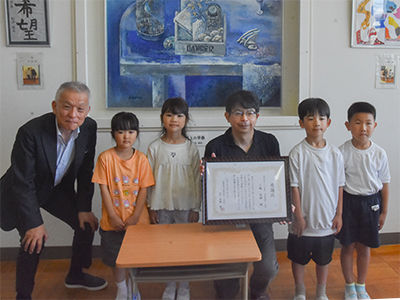 天板を寄贈した三輪・社長と、受け取った児童ら